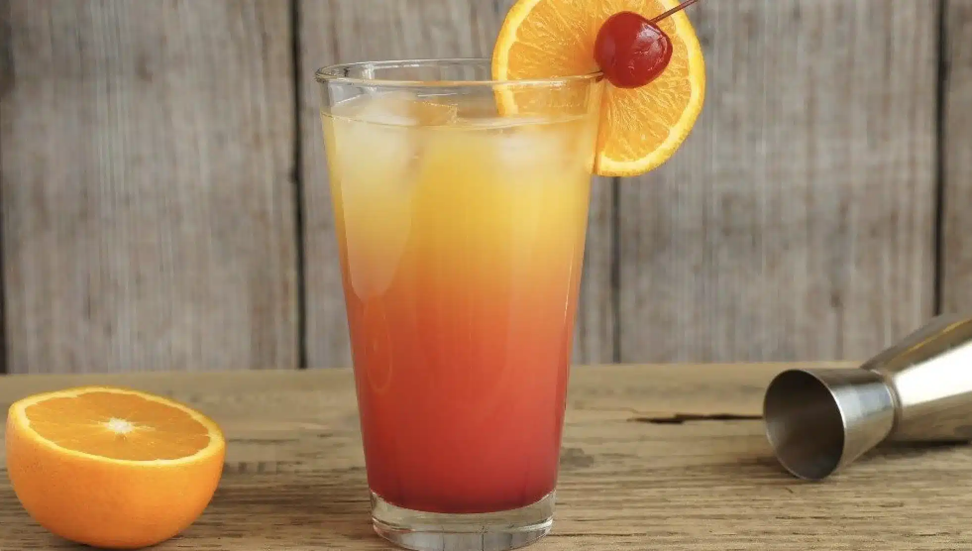 A glass of Corona Sunrise with a cherry on top and an orange on the side