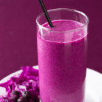 a glass of purple Grimace Shake Recipe on a plate with flowers on the side