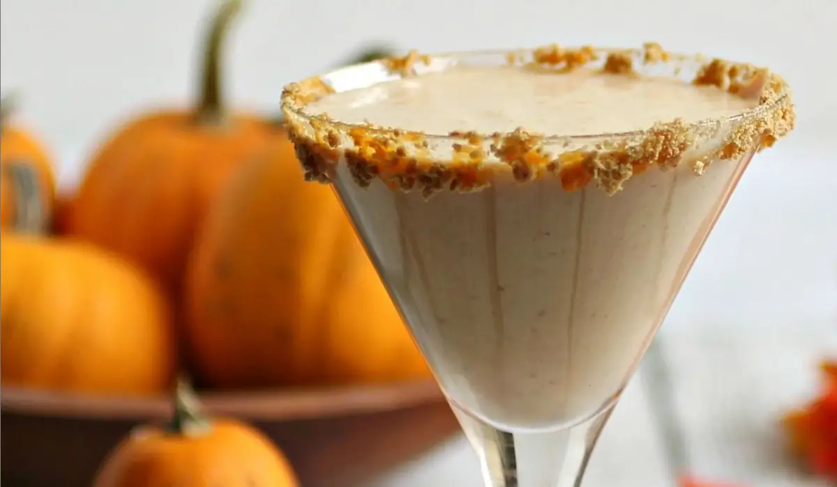 The image features a Pumptini Recipe with a creamy, beige-colored beverage, likely a Pumptini spice cocktail or dessert drink, garnished with a crumbly, golden-brown rim that could be crushed graham crackers or similar toppings.