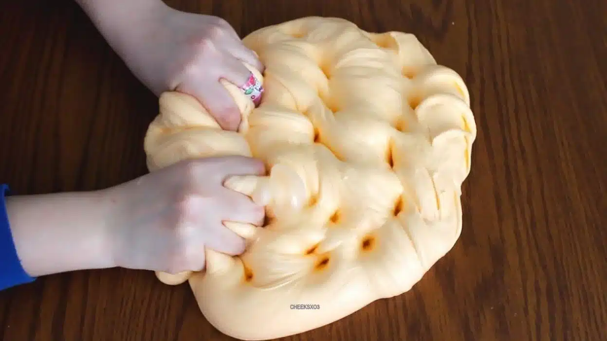 The image captures two hands engaged in the act of squishing and pressing a large butter slime without borax.