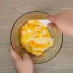 The image shows a hand using a spatula to mix Butter Slime in a clear glass bowl.