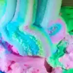 The image features a close-up of a cloud slime with a pastel rainbow of colors, including shades of blue, pink, and green. The texture appears soft and pillowy, reminiscent of cotton candy or some type of whipped dessert.