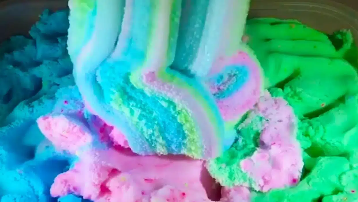 The image features a close-up of a cloud slime with a pastel rainbow of colors, including shades of blue, pink, and green. The texture appears soft and pillowy, reminiscent of cotton candy or some type of whipped dessert.