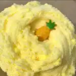 The image showcases a close-up of a swirled yellow confection, possibly a cloud dough slime, with a small, decorative pineapple-shaped piece nestled in the center.