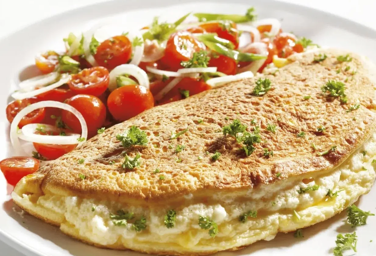 The image displays a fluffy omelette, lightly browned and folded over what appears to be a creamy filling, possibly cheese or a soft cheese mixture, garnished with chopped herbs, likely parsley found in wyse guide recipes