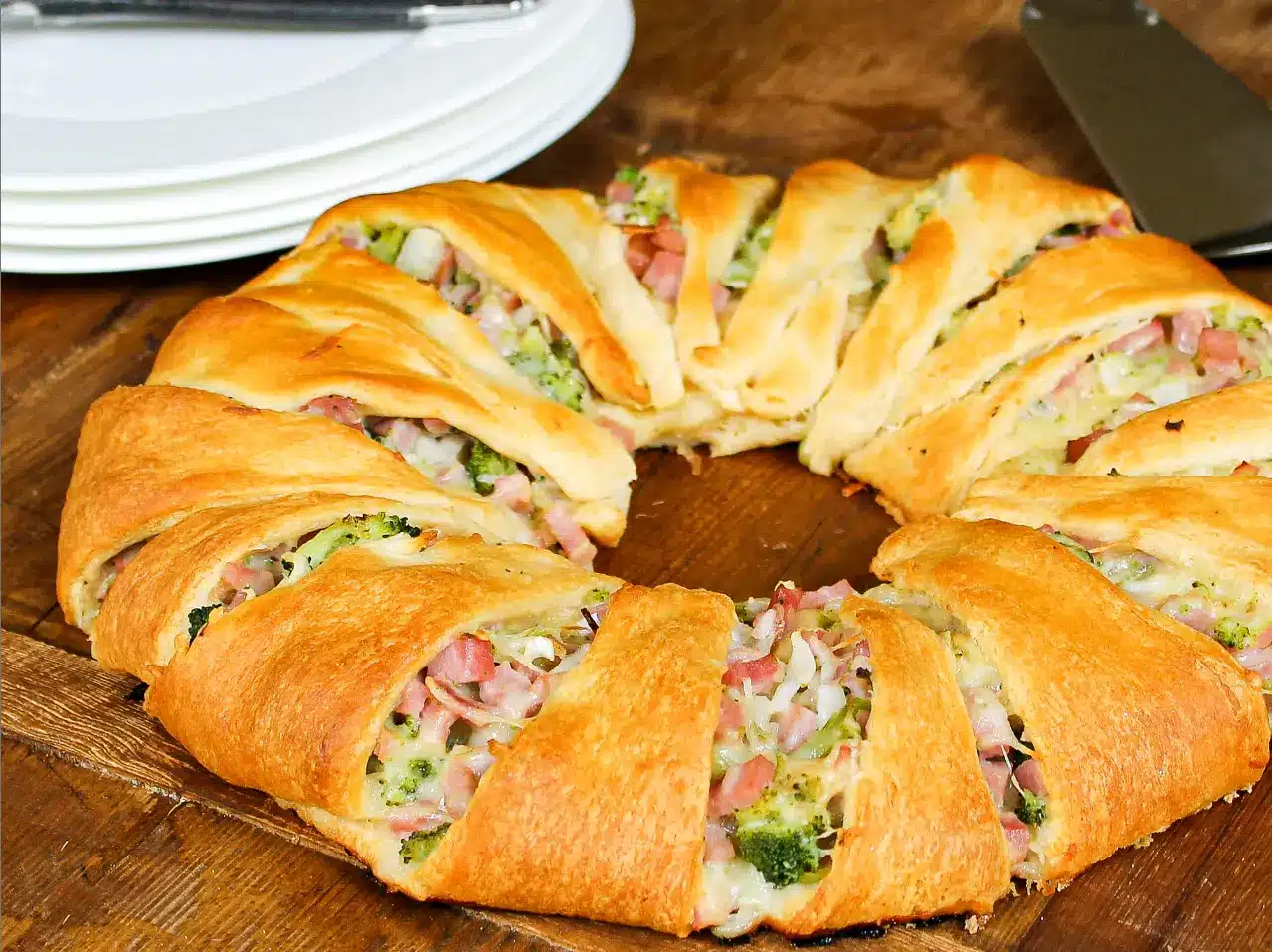 The image shows a freshly baked ring-shaped pastry, likely a crescent roll or similar dough, filled with a mix of ingredients that appear to be ham, cheese, and broccoli from publix recipes