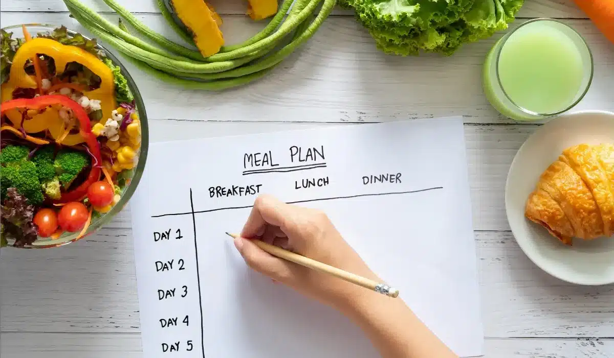The image shows a person's hand writing on a meal plan for publix