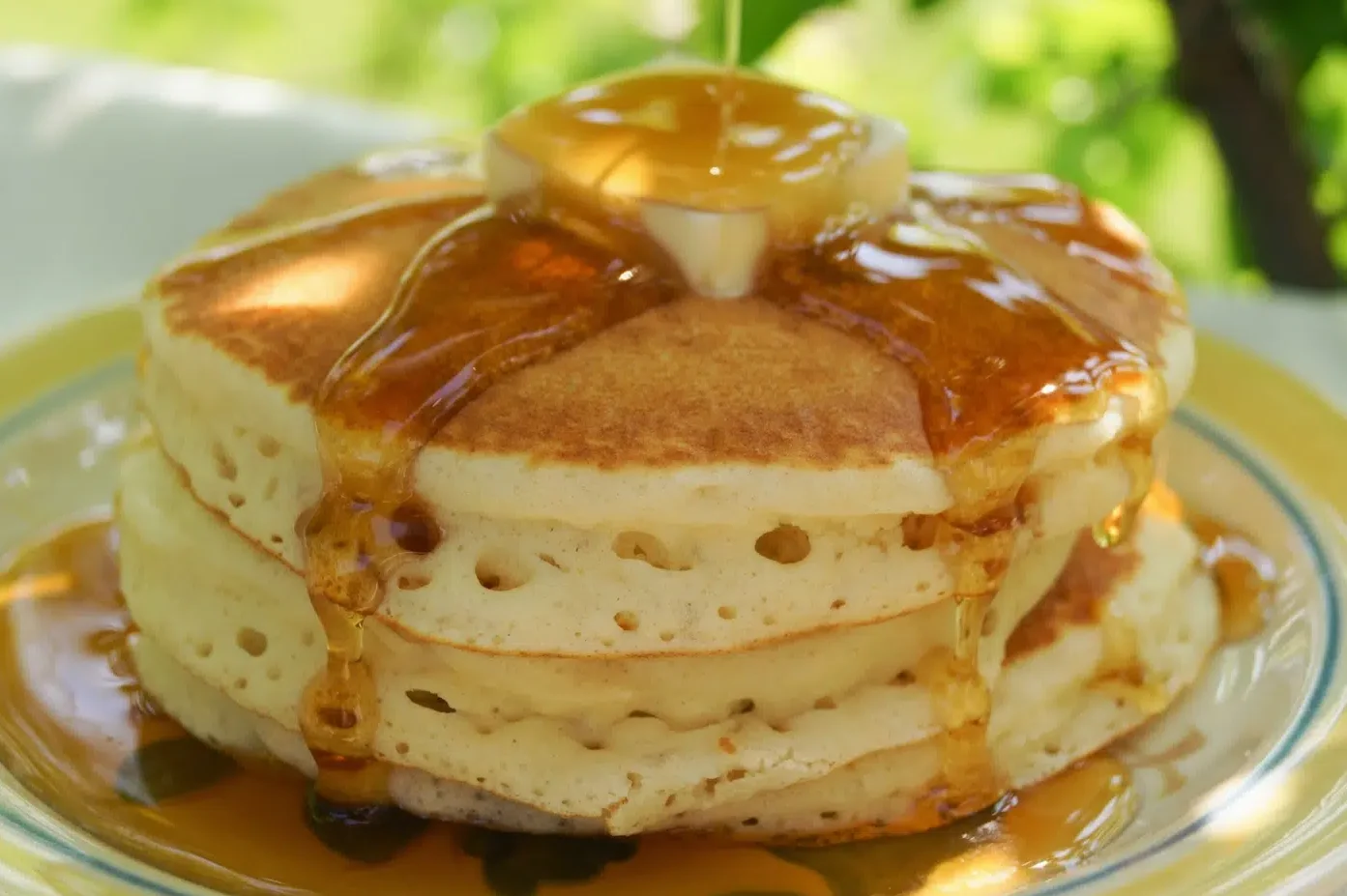 The image displays a stack of fluffy pancakes on a yellow and blue striped plate from Good Morning America Recipes.