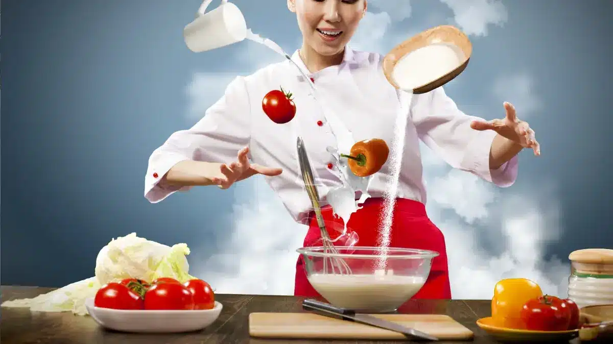 The image depicts a dynamic cooking scene where a smiling cook on from Today show in a white chef's coat and red apron is juggling ingredients mid-air with great skill.
