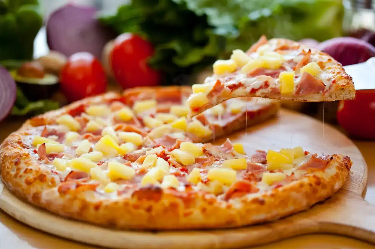 a plate of hawaiian pizza with slice of it being lift off