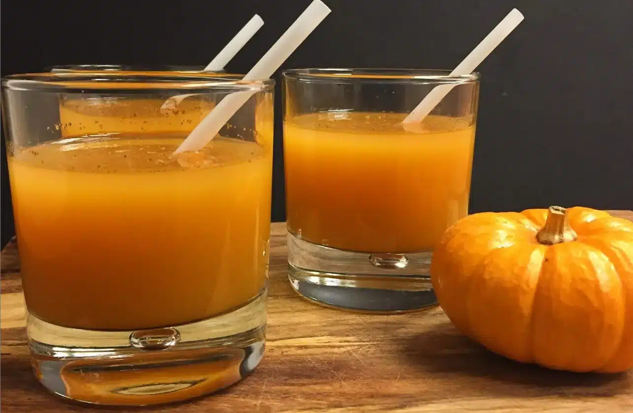 The image displays two clear glasses filled with a vibrant orange liquid, likely to be a Pumptini, with white straws inserted.