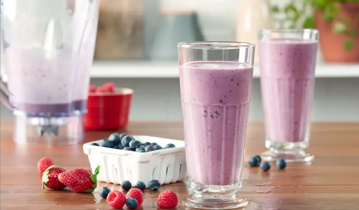 The image shows three tall glasses filled with grimace shake recipe, placed on a wooden surface.