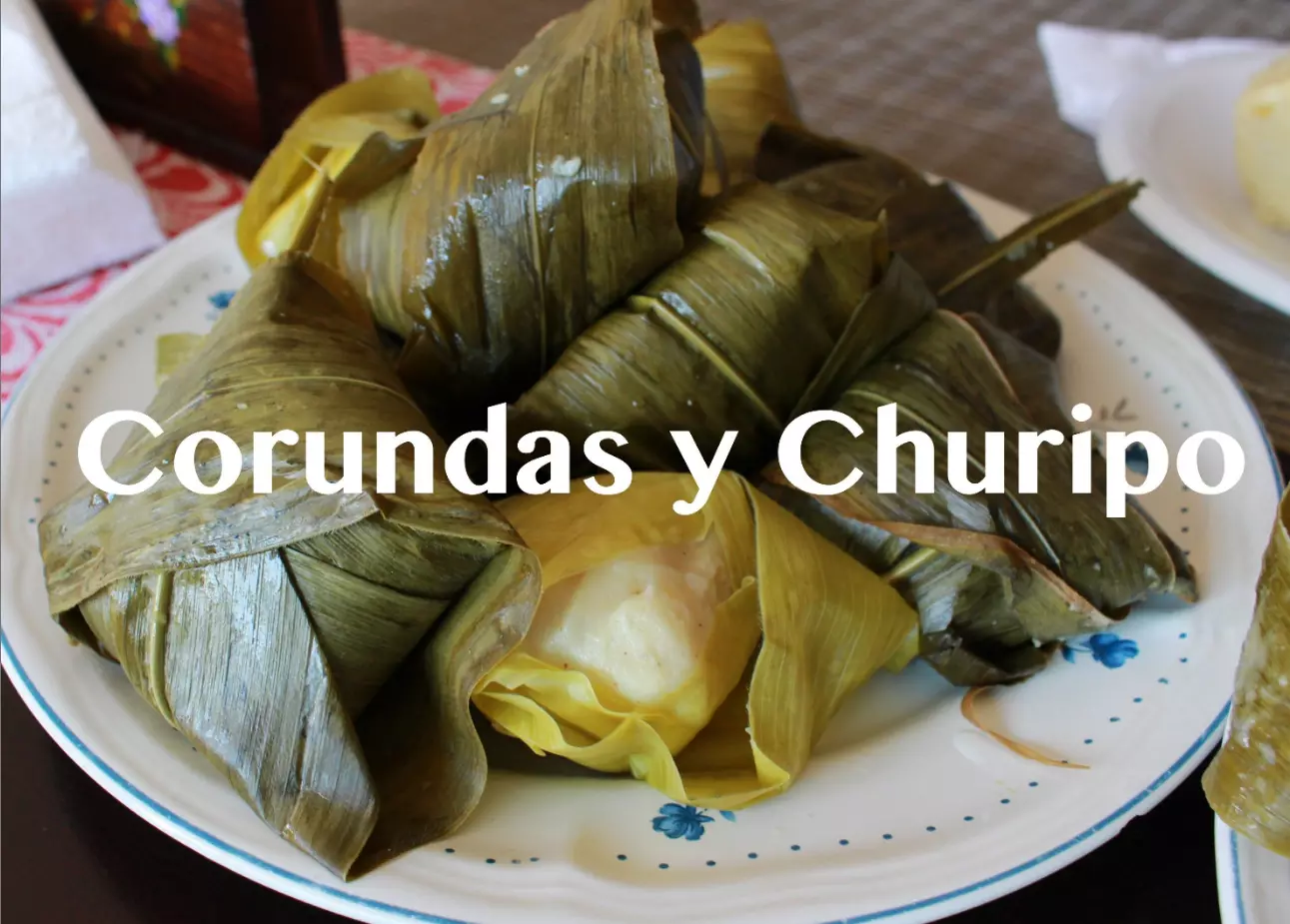 A plate of two corn husk-wrapped tamales with a small bowl of corundas