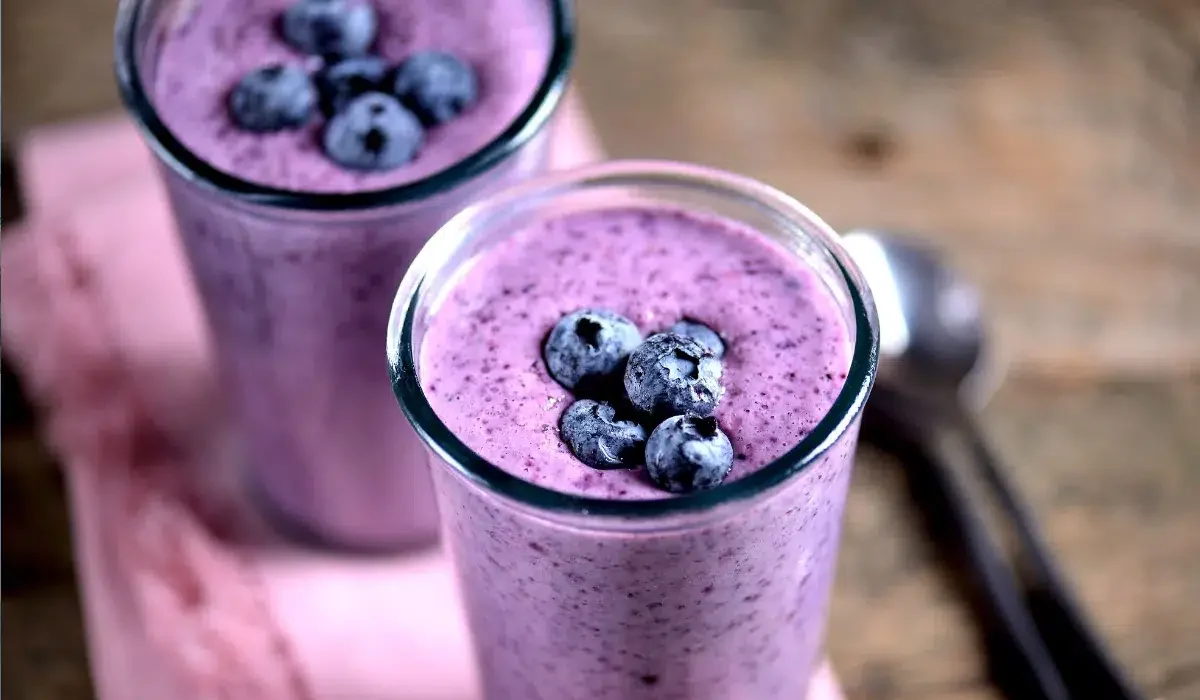 The image showcases two glasses of grimace shake with a rich purple hue, topped with a handful of whole blueberries.