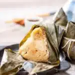 A close up of a rice dumpling wrapped in a green leaf on a plate called Corundas