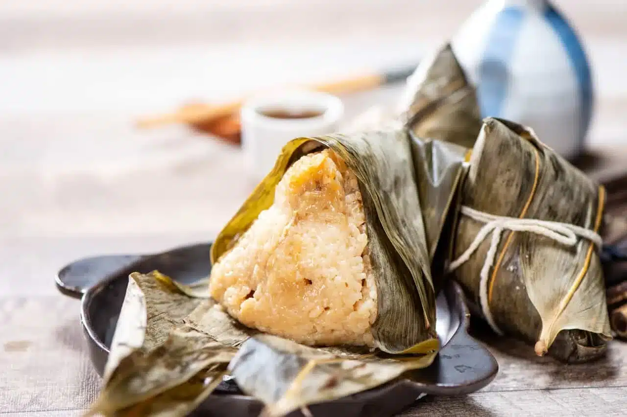A close up of a rice dumpling wrapped in a green leaf on a plate called Corundas