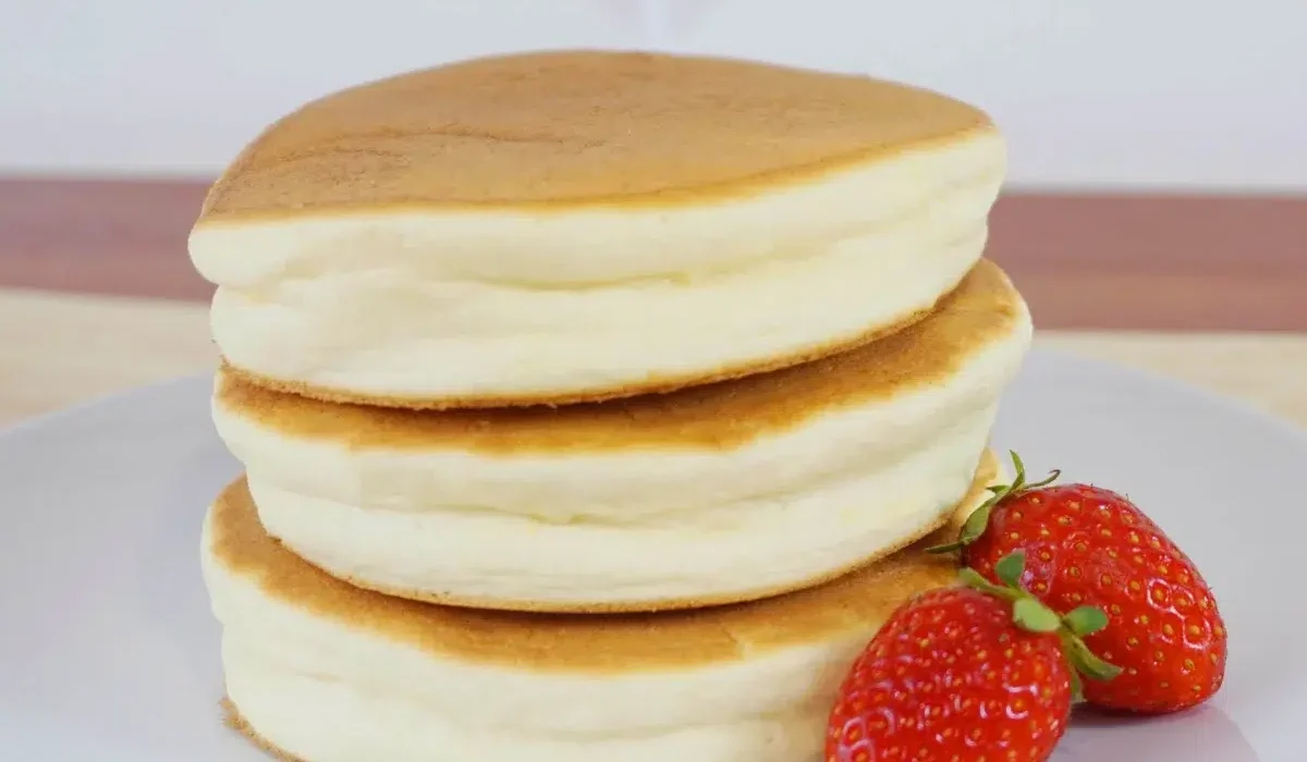 The image displays a stack of three fluffy, thick pancakes on a white plate.