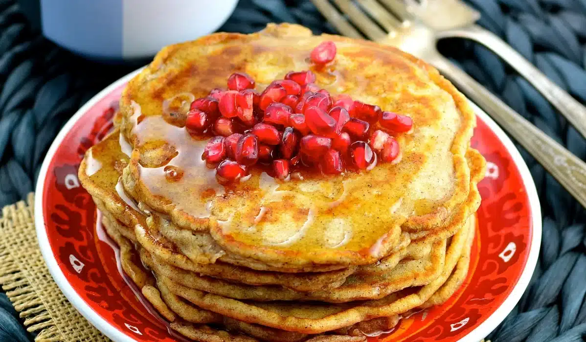 Image of a stack of pancakes with syrup and pomegranate seeds on a red plate for Pound Dropper Recipes