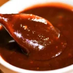 This is an image of a dark, rich Bloves sauce in a white bowl with a spoon lifting some out, indicating a thick and possibly sticky texture.