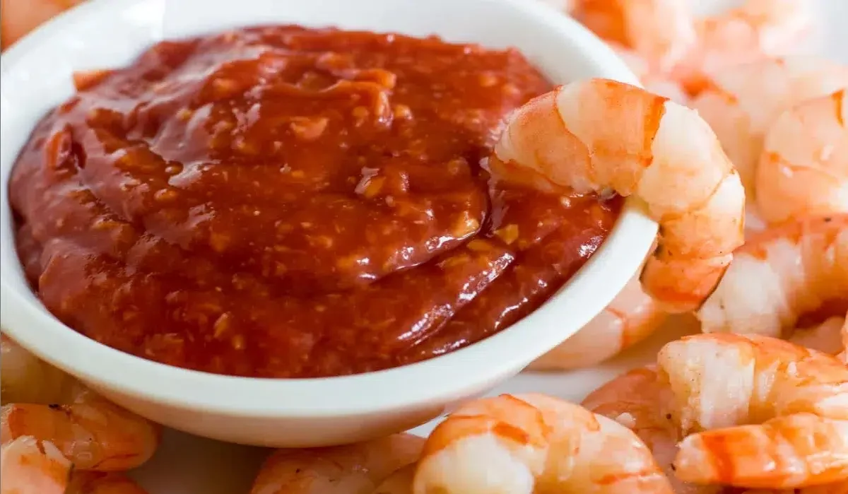 The image shows a plate of cooked shrimp arranged in a circle around a bowl of red sauce, which appears to be a seafood boil sauce