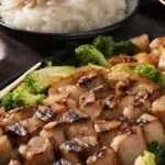 Grilled cubed meat, likely Blackstone Hibachi Recipe, with a glossy glaze, presented on a black plate with a side of white rice and bright green broccoli