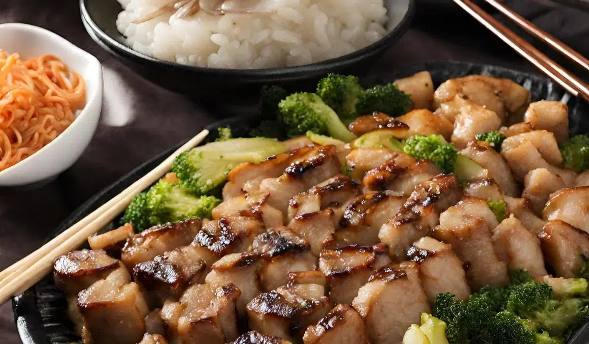 Grilled cubed meat, likely Blackstone Hibachi Recipe, with a glossy glaze, presented on a black plate with a side of white rice and bright green broccoli