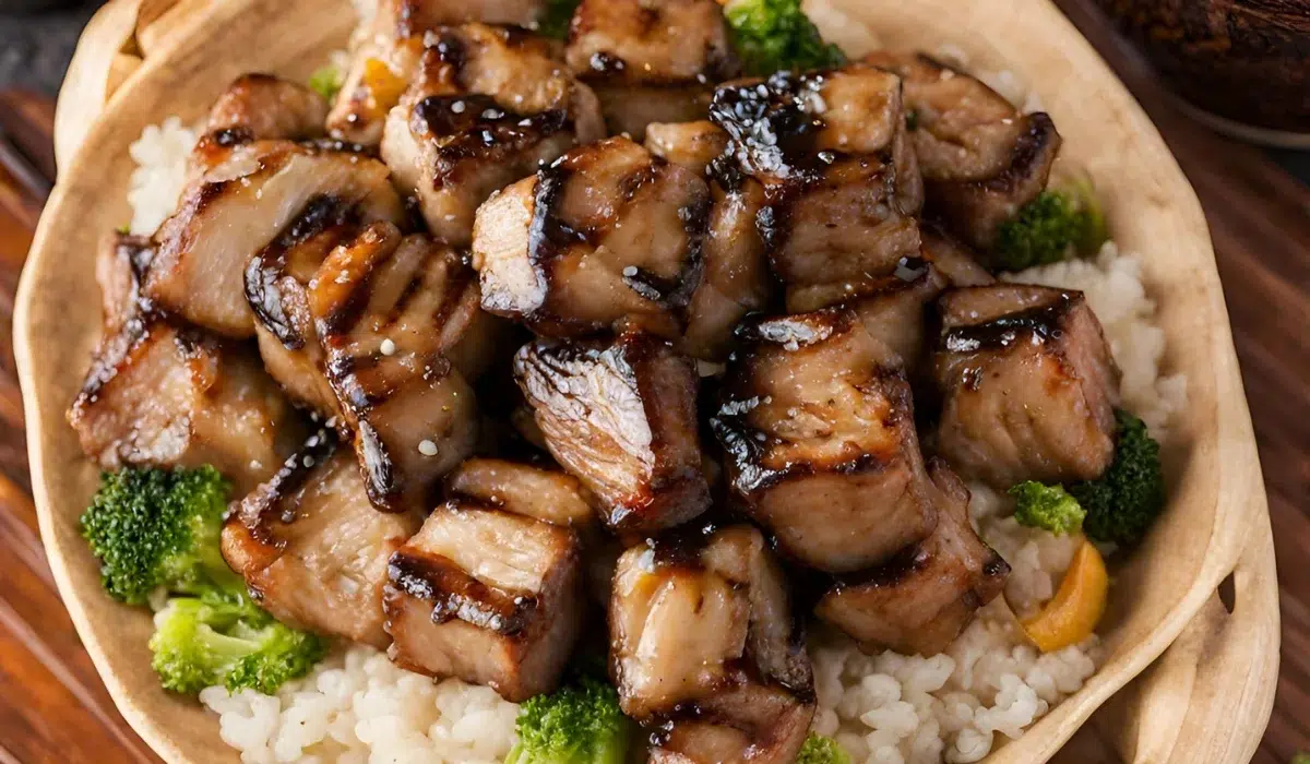 Here, the grilled hibachi is arranged on a wooden platter over a bed of white rice, with hibachi oil