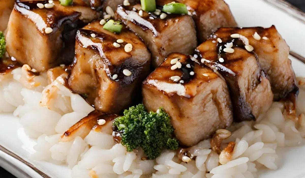 This presentation features the glazed hibachi atop a bed of white rice on a rectangular plate. likely made by Chefs Squirt On Food