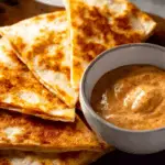 Bowl of creamy jalapeño sauce next to melted quesadilla wedges